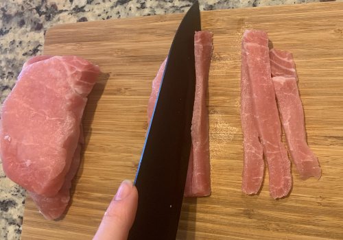 Pork chop being sliced into long, narrow strips