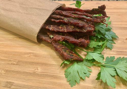 Beef jerky in an open paper bag beside fresh cilantro