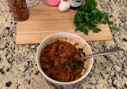 Beef strips in a bowl of red marinade flecked with herbs