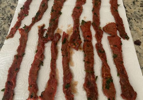 Herb-coated beef strips draining on paper towels