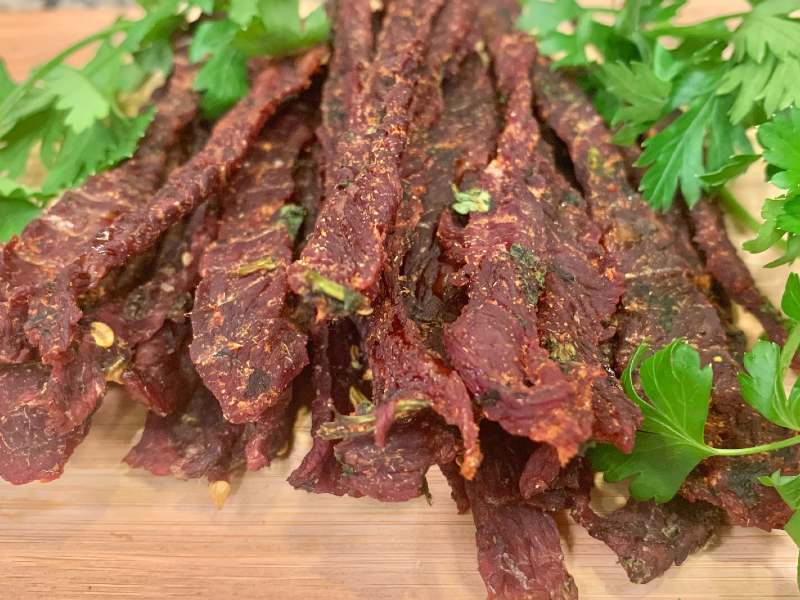 Beef jerky strips scattered with herbs beside fresh cilantro