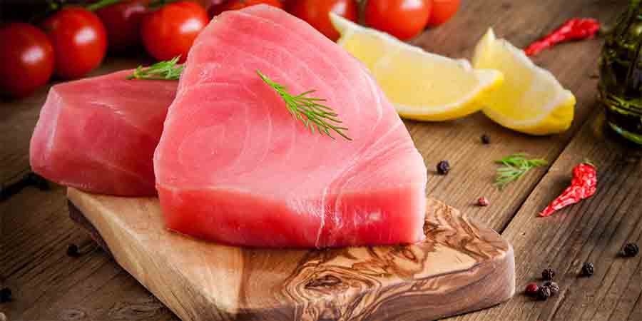 Raw tuna steaks on a board with lemon and herbs