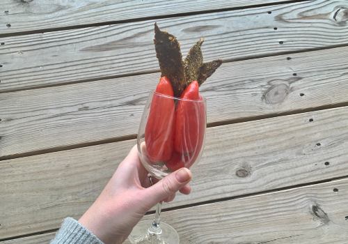Hand holding a glass with beef jerky strips and a red pepper