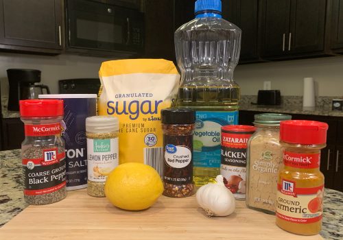 Lemon, garlic, sugar, oil and bottled seasonings on a cutting board