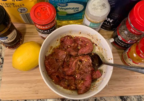Beef slices in a bowl of marinade surrounded by seasonings