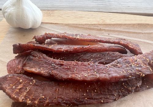 Beef jerky strips on a board beside garlic