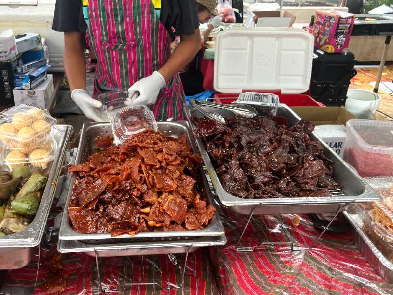 Vendor serving dried meat from trays at a market stall