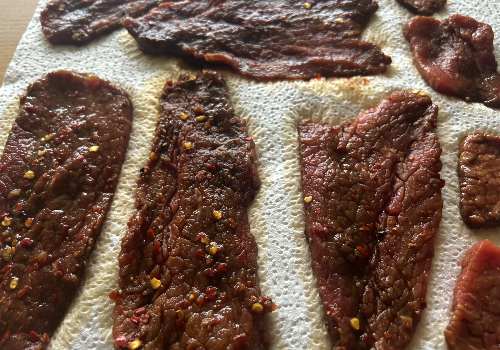Pepper-flecked marinated beef strips draining on paper towels