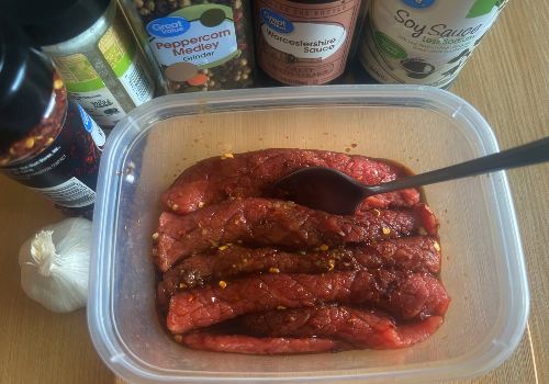 Beef strips in a seasoned marinade inside a container