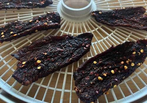 Dark dried beef jerky on a dehydrator tray