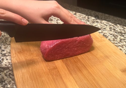 Hands slicing a piece of raw beef on a board