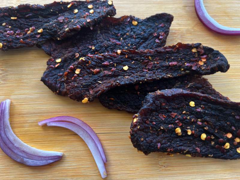 Dark beef jerky with crushed red pepper beside slices of red onion